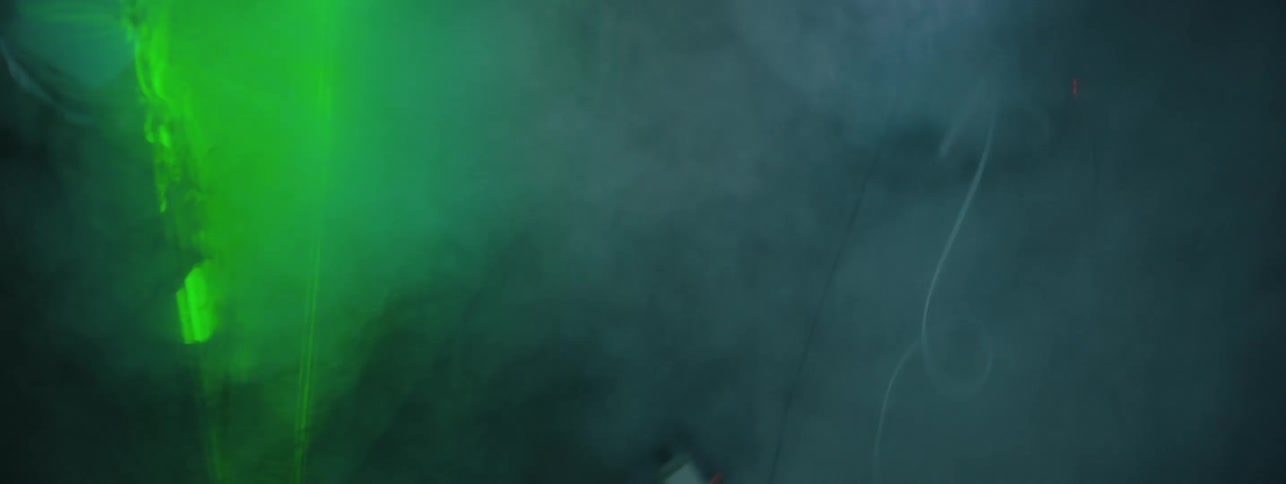The man gets up from the ground in the foggy room with a green strobe light