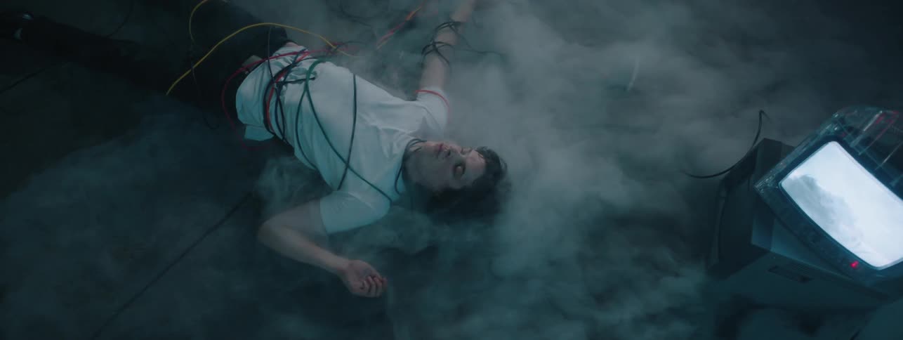 Smoke floats around a man bound in cables on the floor