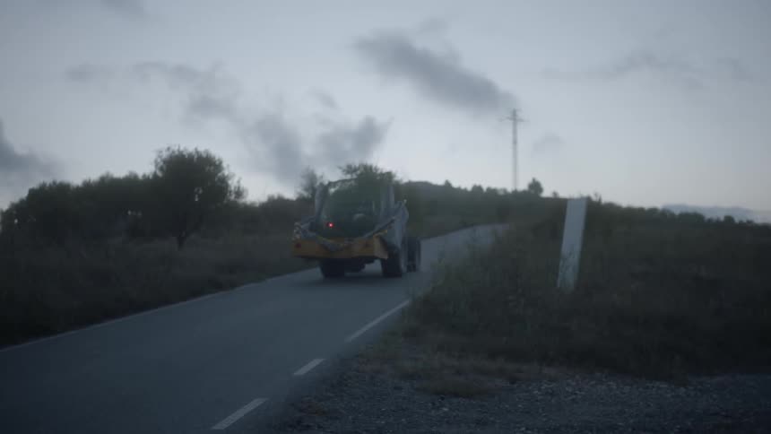 Person is driving tractor on country road at dusk