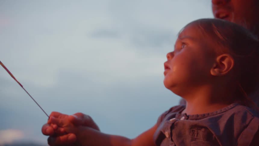 The child is waving a sparkler with the help of a man