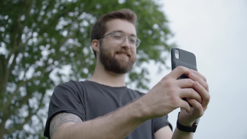 Bearded man smiles as he holds his cellphone in front of his face
