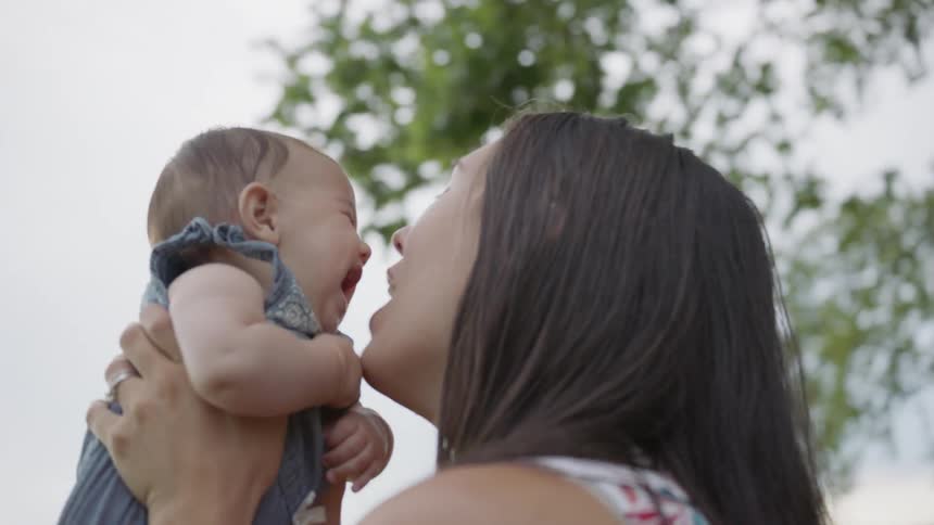 Baby laughs as a woman holds it and kisses it