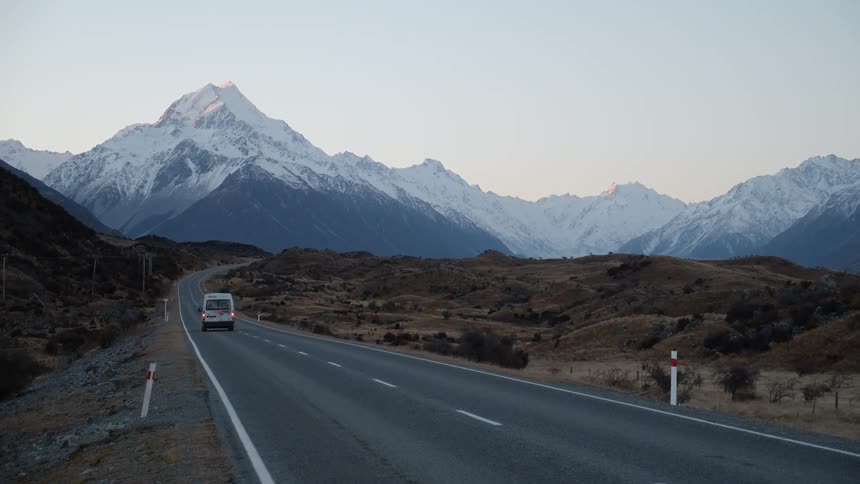 A van drives down a winding road toward a mountain at sunset