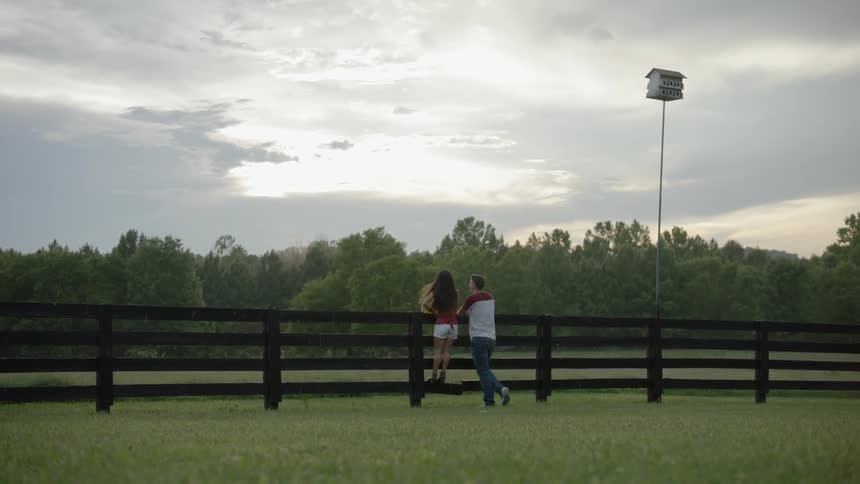 The woman climbs on the wooden fence by the man