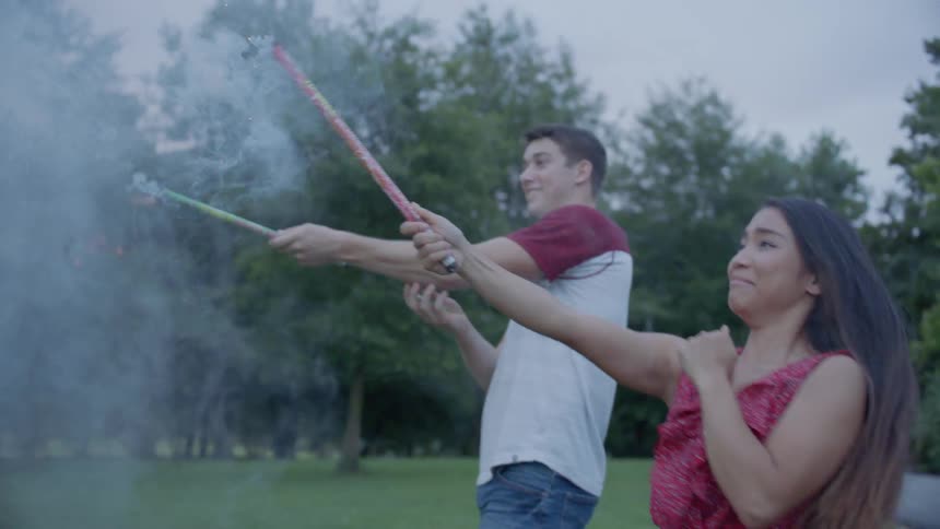 The man and woman shoot off roman candles together in the grass