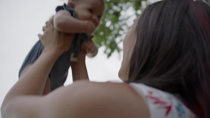 The baby laughs as the woman tosses him in the air