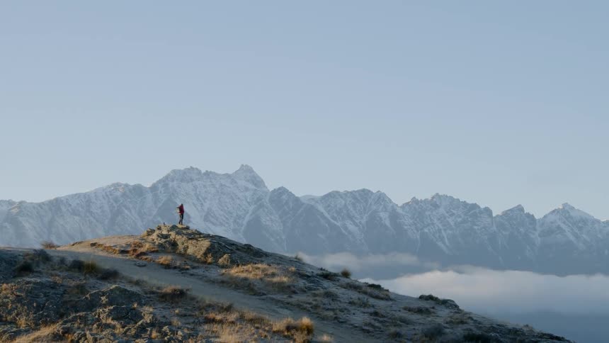 A hiker stands on a rocky ridge looking out at clouds and peaks