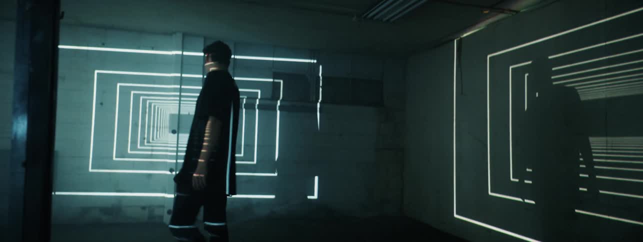 A teenage boy is walking in a room as lights cast a geometric pattern on the walls