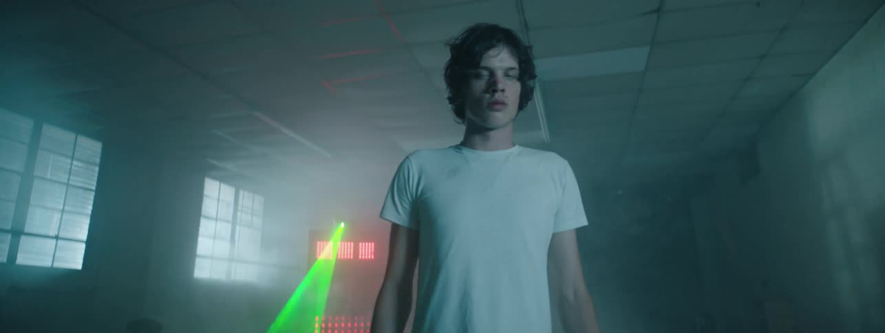 A piece of equipment shines a green laser light in a room where a boy walks through smoke
