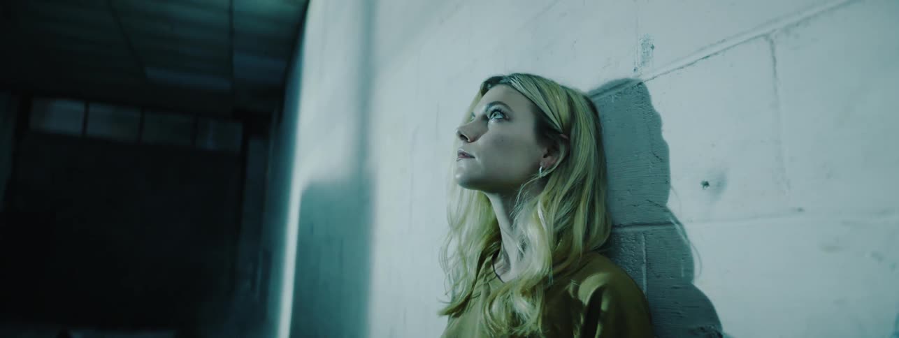 Blond woman leans against a cement wall
