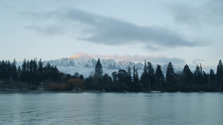 Water is rippling in lake in front of trees and snowy mountain wilderness