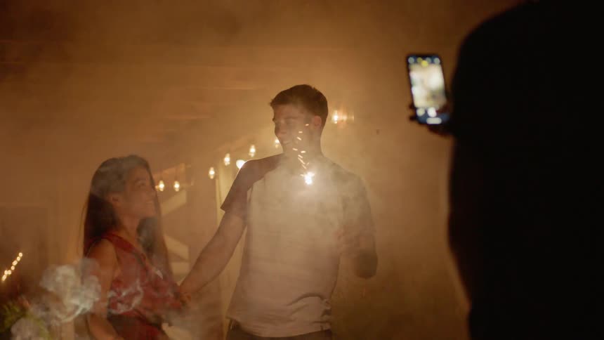 The couple swing sparklers and kiss in the yard