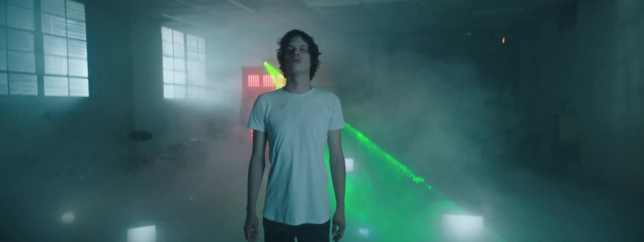 A laser light moves back and forth as teenage boy walks through a smoke filled room