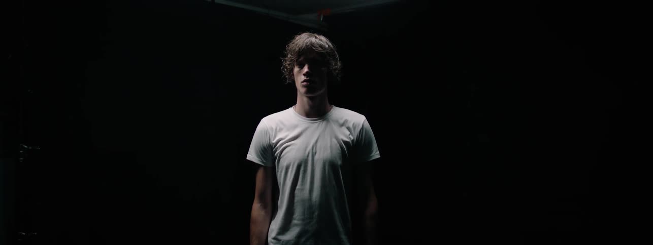 Man in a white shirt stands in the dark