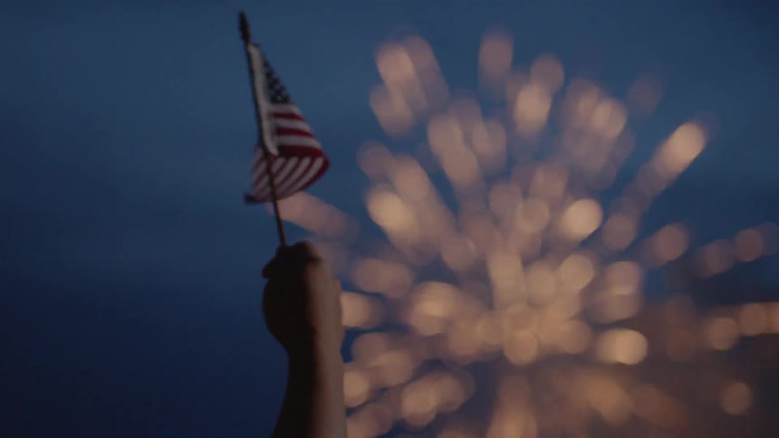 The person waves an american flag as the fireworks go off