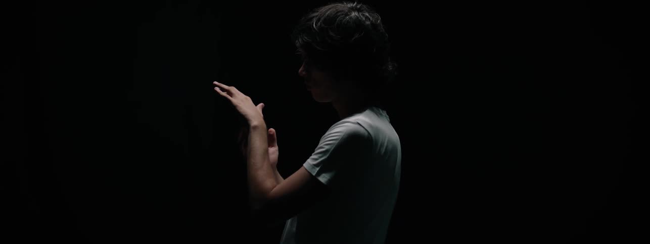 Man stands in darkness gazing at his hands