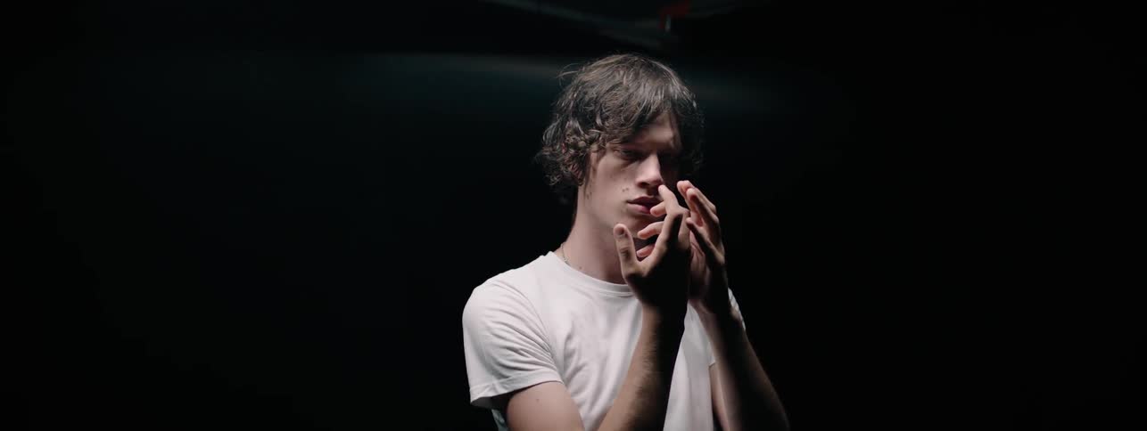 Man in a white shirt looks at his hands as he moves them around
