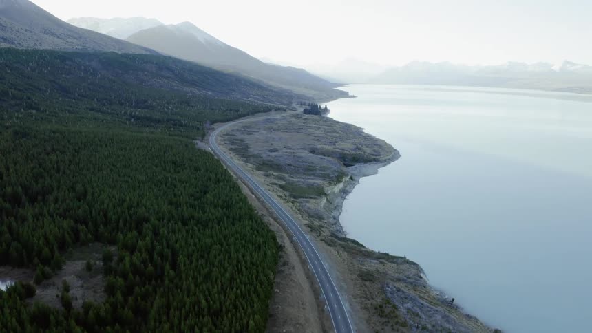 A narrow road runs along a coastline in a mountainous setting in daylight