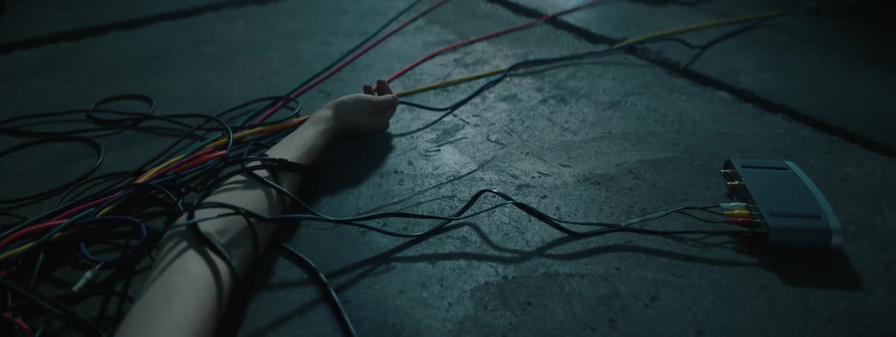 Person with wires wrapped around arm lays still on concrete floor