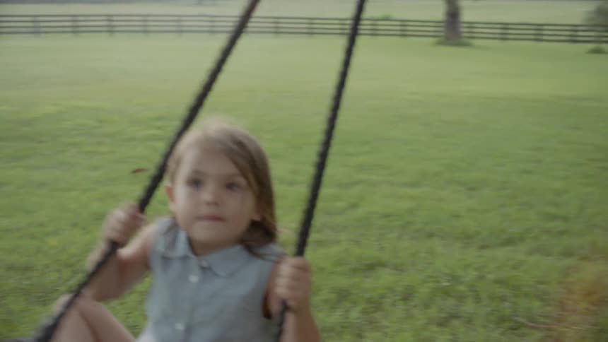 A father pushes a young daughter on a rope swing