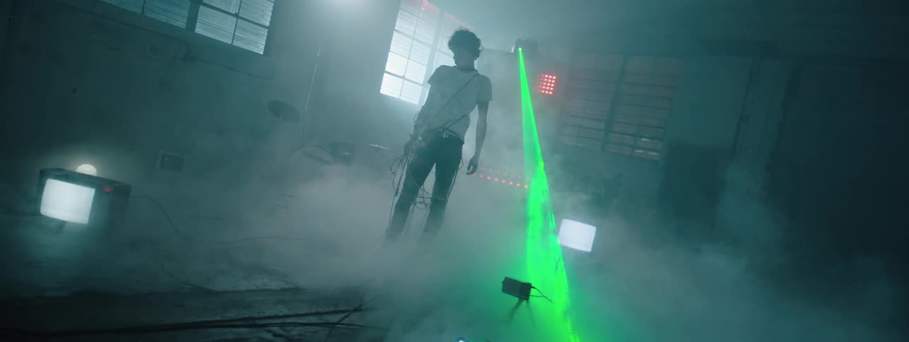 The man has a green strobe light shining on him in the foggy room