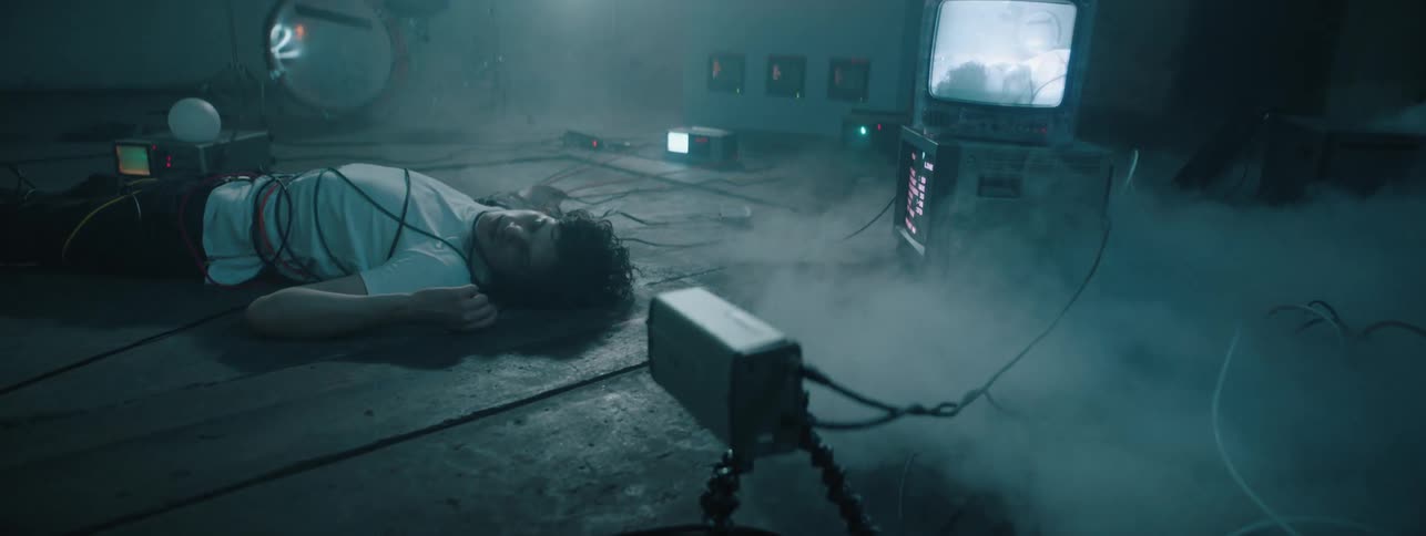 Smoke swirls around a man bound in cables on a warehouse floor