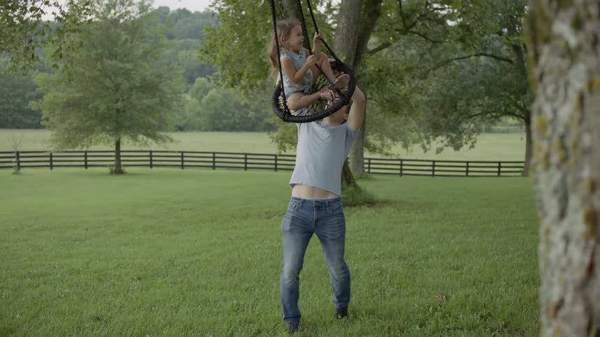 The man pushes the child in the swing on the tree