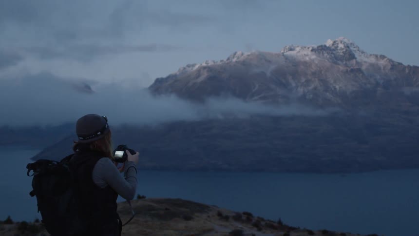 Man stands on mountain top near river and takes photos