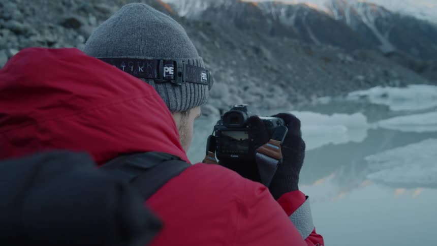 A man turns his camera as he takes a photograph of the icy water and mountains