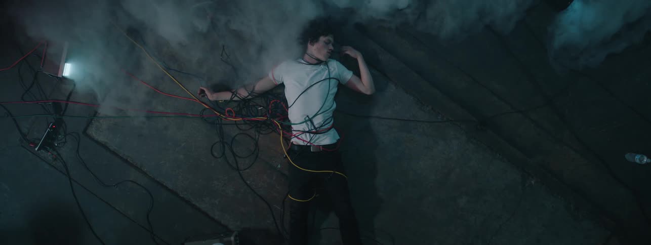 The man lies on the ground covered in wires and fog