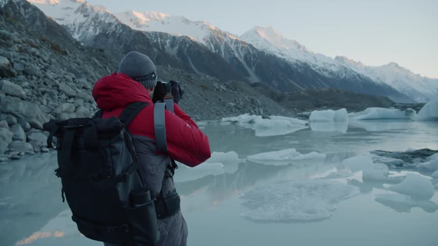 A female photographer carrying a backpack is taking photos of a glacier and icebergs in daylight