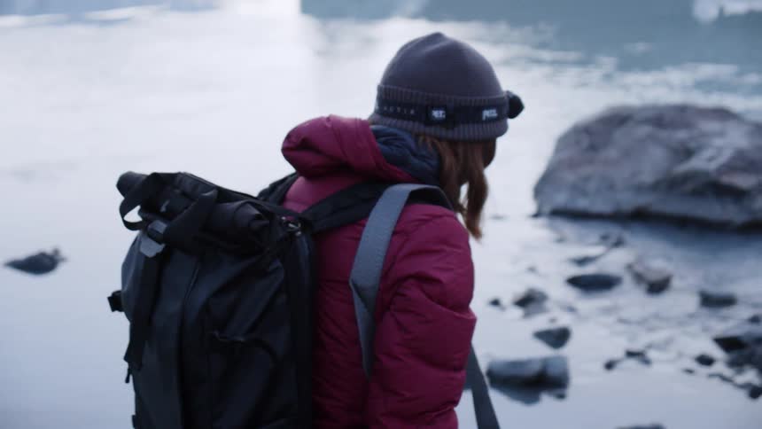 A woman wears a backpack while hiking near an icy lake