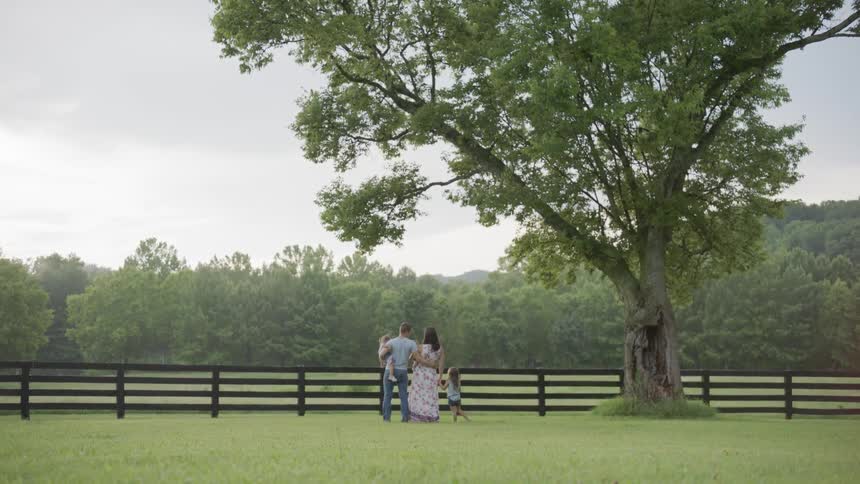 The family stand together by a large tree near the fence