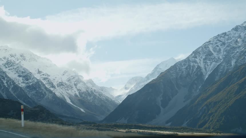 Snow capped mountains with a partly cloudy sky alongside a roadway