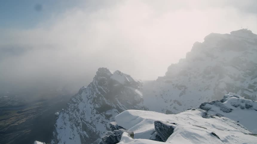 Mist floats over the snow covered mountains under a cloudy blue sky
