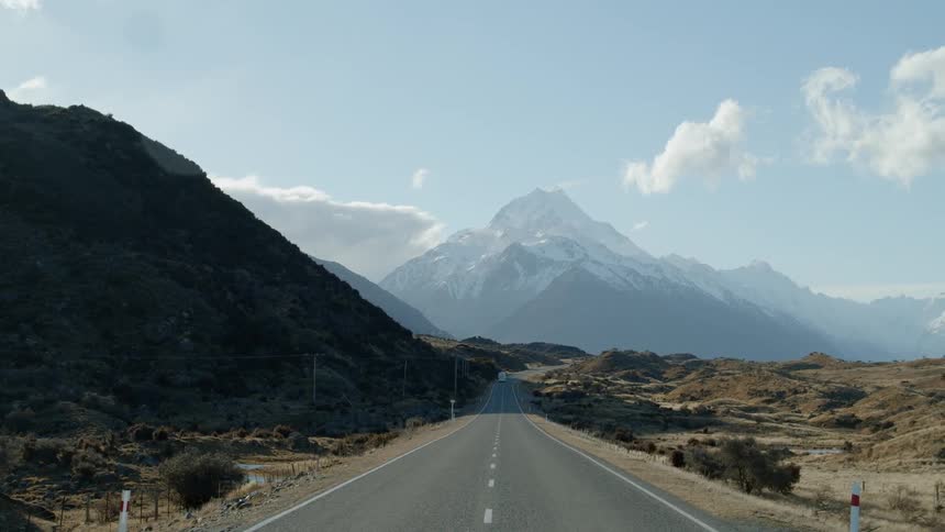Snow-capped mountains loom beyond a rural road on a sunny day