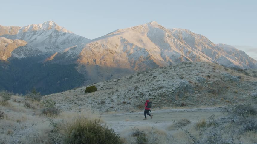 The person is hiking towards the mountains on a cloudy day