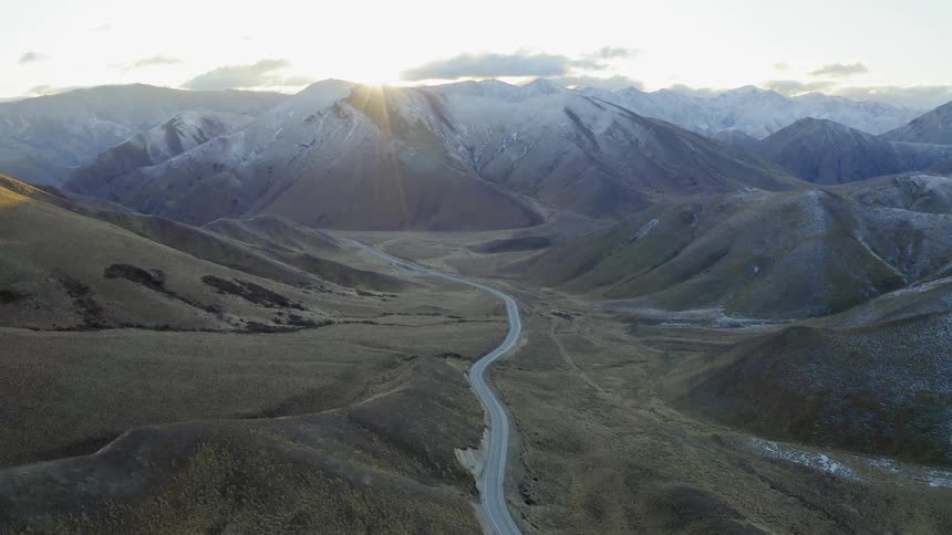 The road runs through the middle of the mountain range at sunset