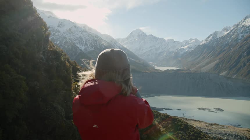 Woman wearing a red jacket looks out at the snow covered mountains