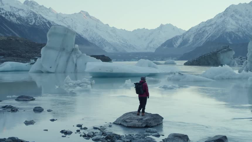 A person on a rock next to some icebergs looking at mountains