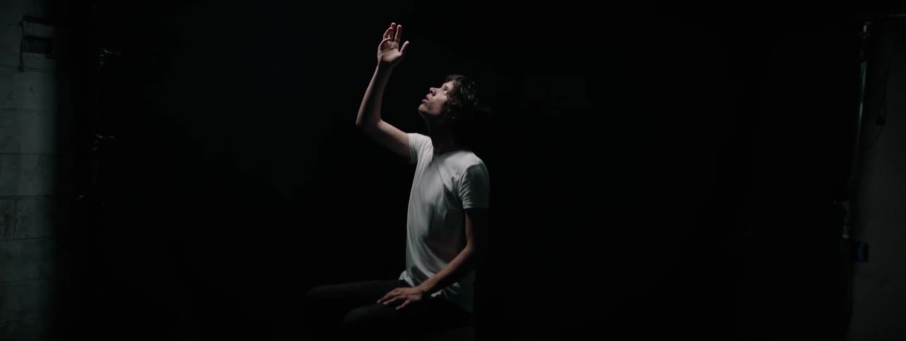 Man looks up and raises his hand up in a dark room