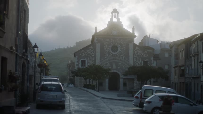 Cars parked along a small road in a town with a church on a cloudy but bright day