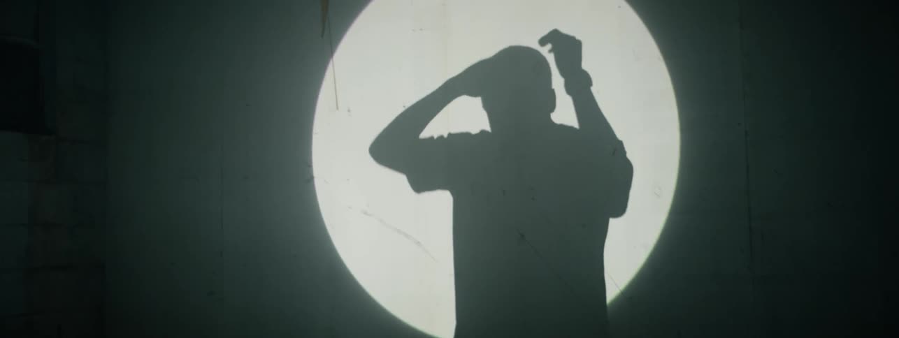 The shadow of a man can be seen in the spotlight on the wall