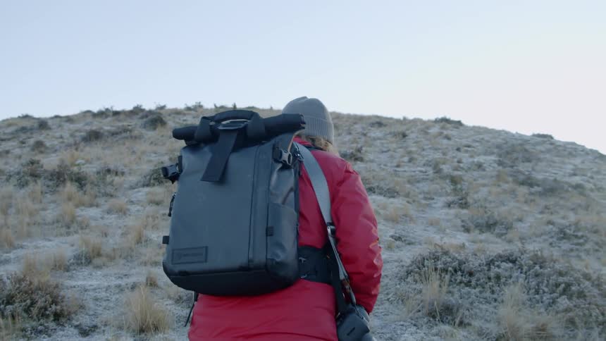 A female photographer is hiking up a hill carrying a backpack in daylight