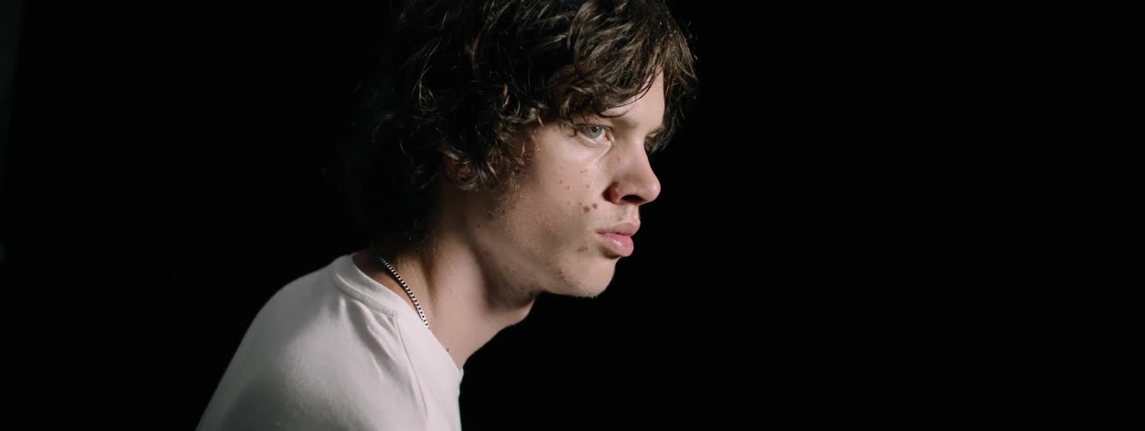 Man in a white shirt blinks his eyes in a dark room