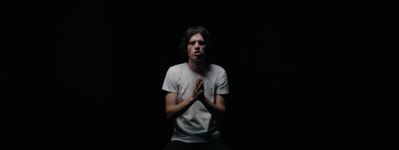 A man rubs his hands over his face in a dark room