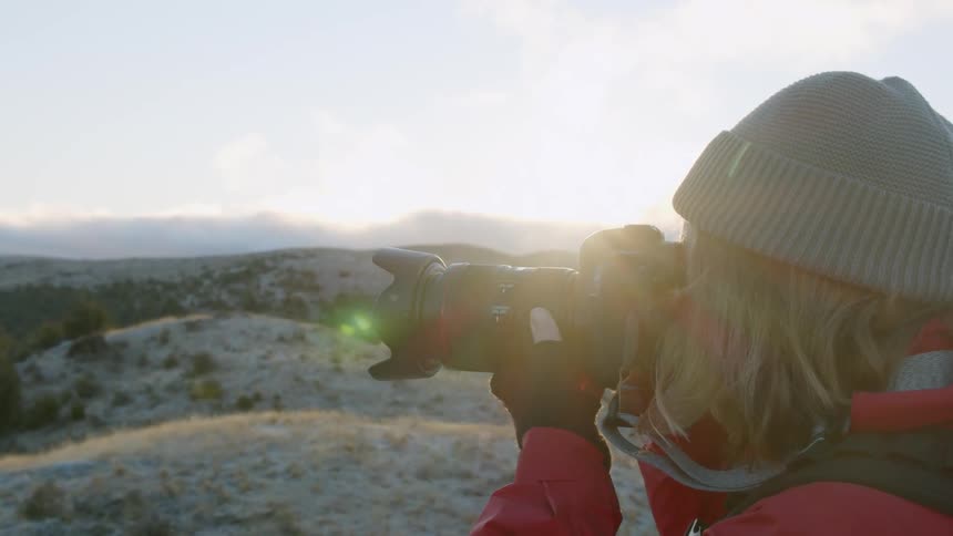 Woman is photographing scenery in mountain wilderness at sunset