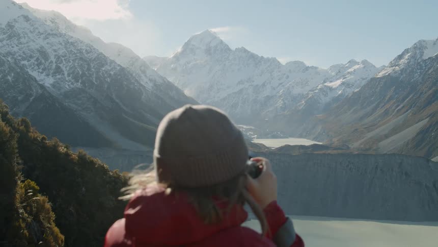Woman taking a picture of a mountain range surrounding a lake