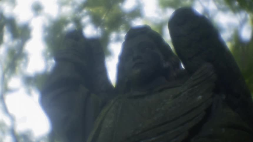 Sunlight shines behind a stone angel statue