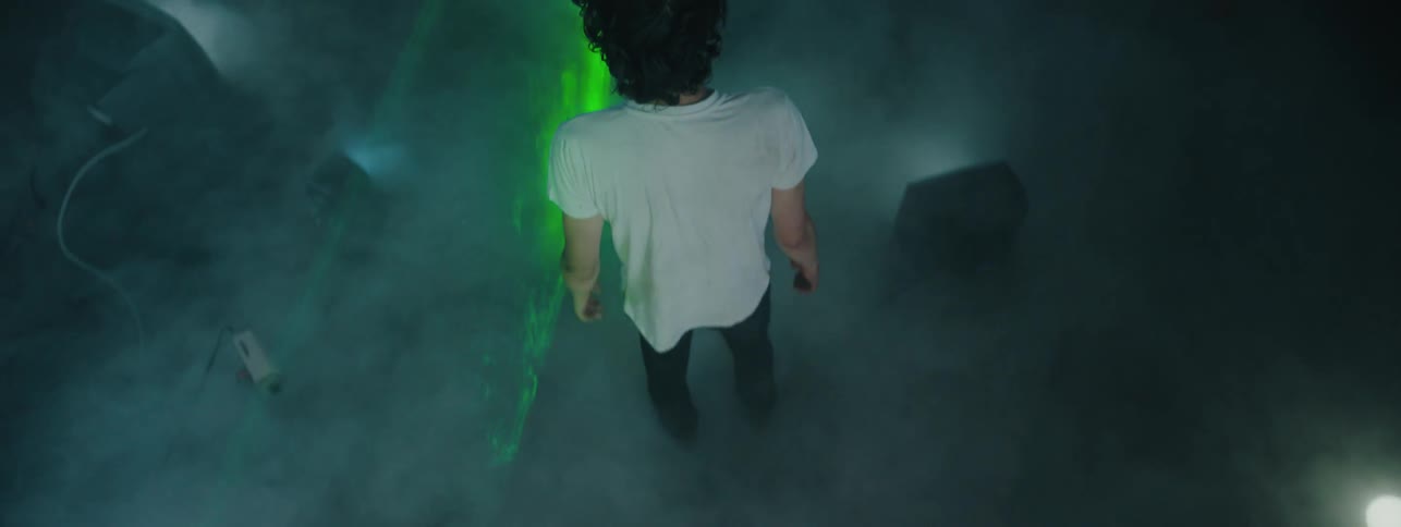 The man is standing in a room covered in fog and a green strobe light